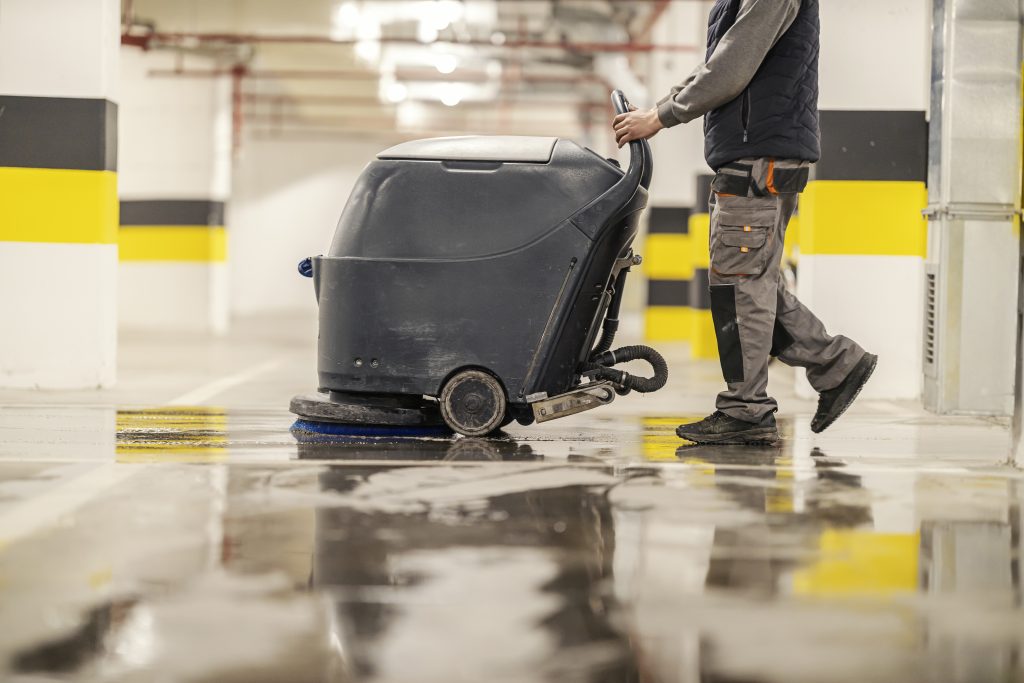 side view of an unrecognizable worker washing public garage with washing machine.